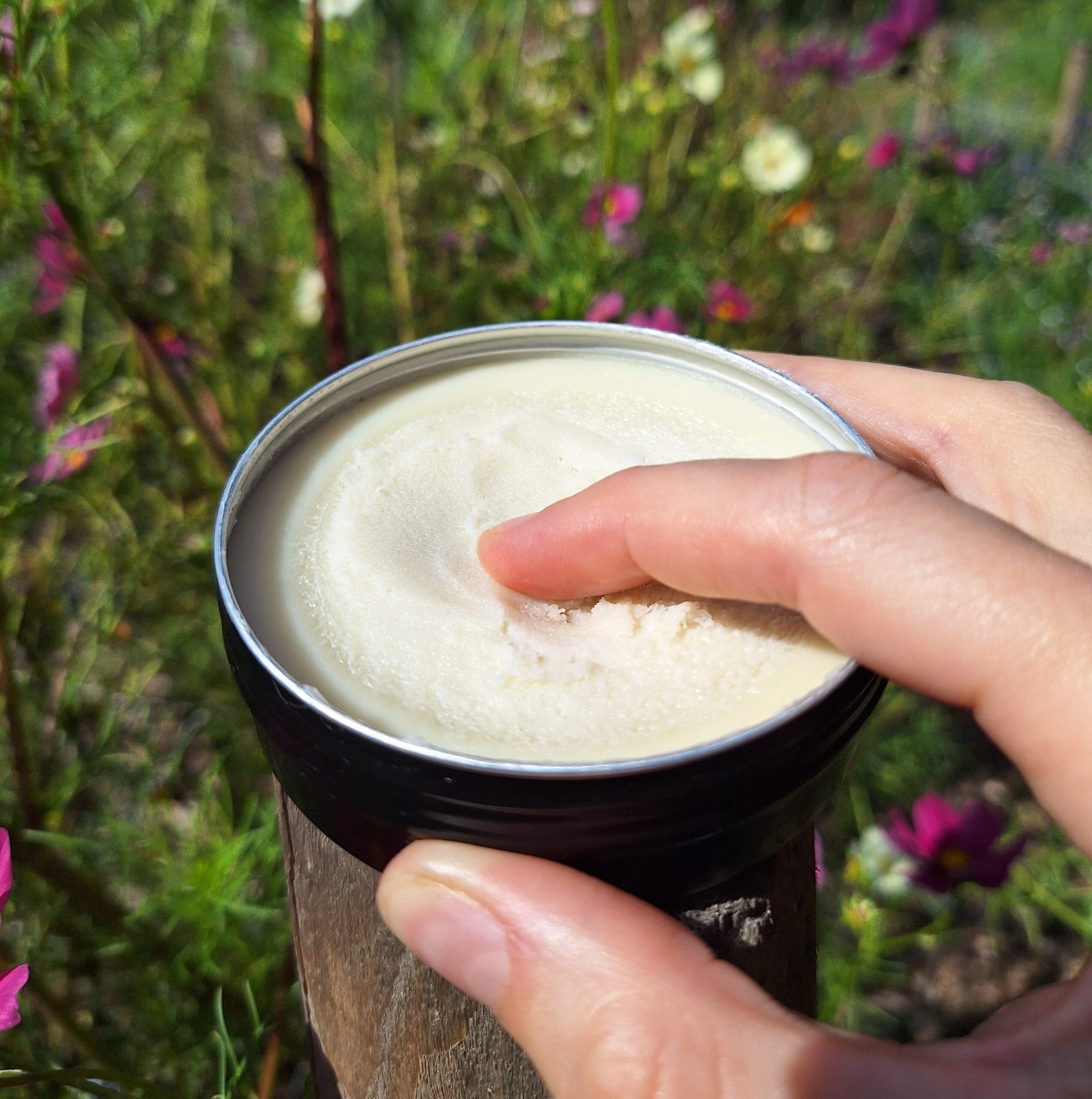 Hand smeert natuurlijke crème op huid in bloementuin
